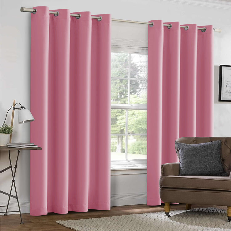 Pink curtains hanging in a room with a window and a sofa.