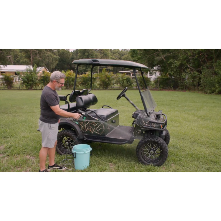 Man standing next to a golf cart on a grassy area with trees in the background