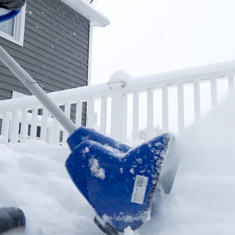 Blue snow shovel with snow on a white railing and house in the background