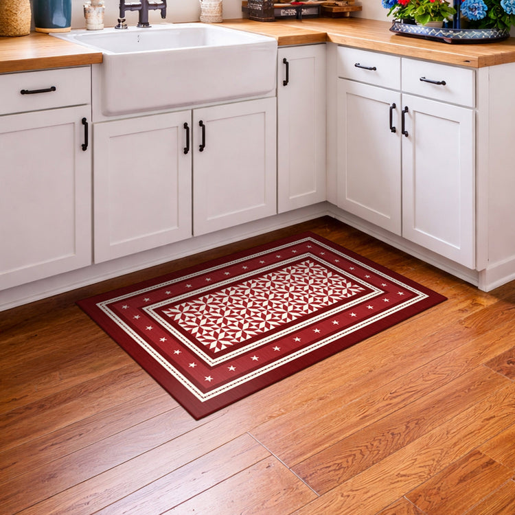Decorative red and white patterned rug on a wooden floor in a kitchen.