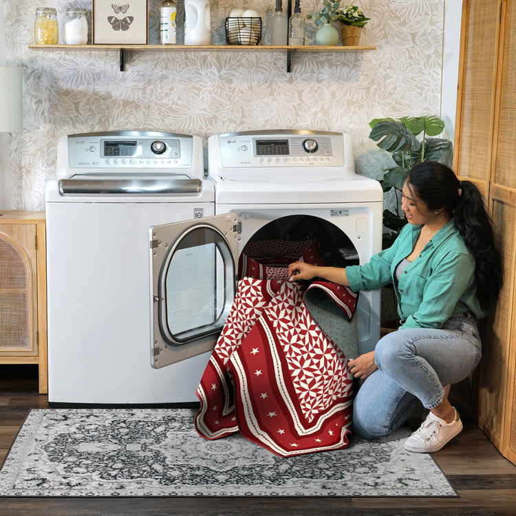 Woman taking a red and white patterned towel out of a dryer in a laundry room.