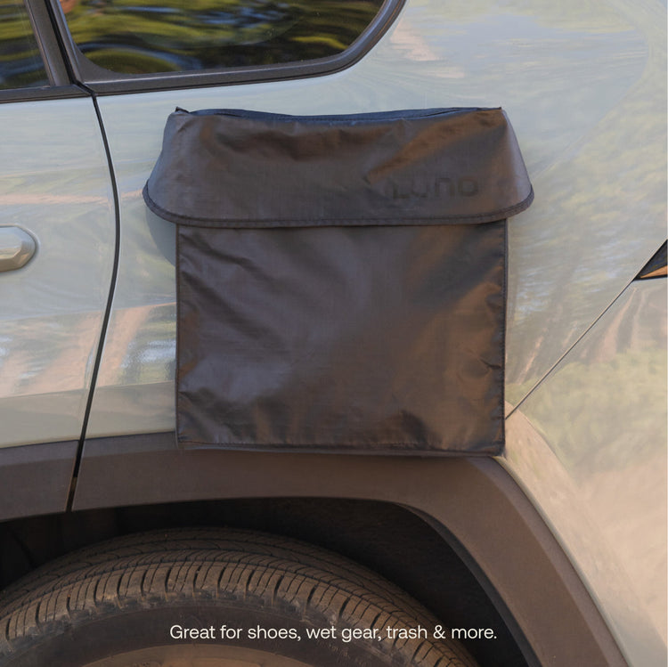 A black Luno® Gear & Shoe Storage Bag is attached to the rear side door of a silver vehicle, offering water-resistant storage for shoes, wet gear, trash, and more.