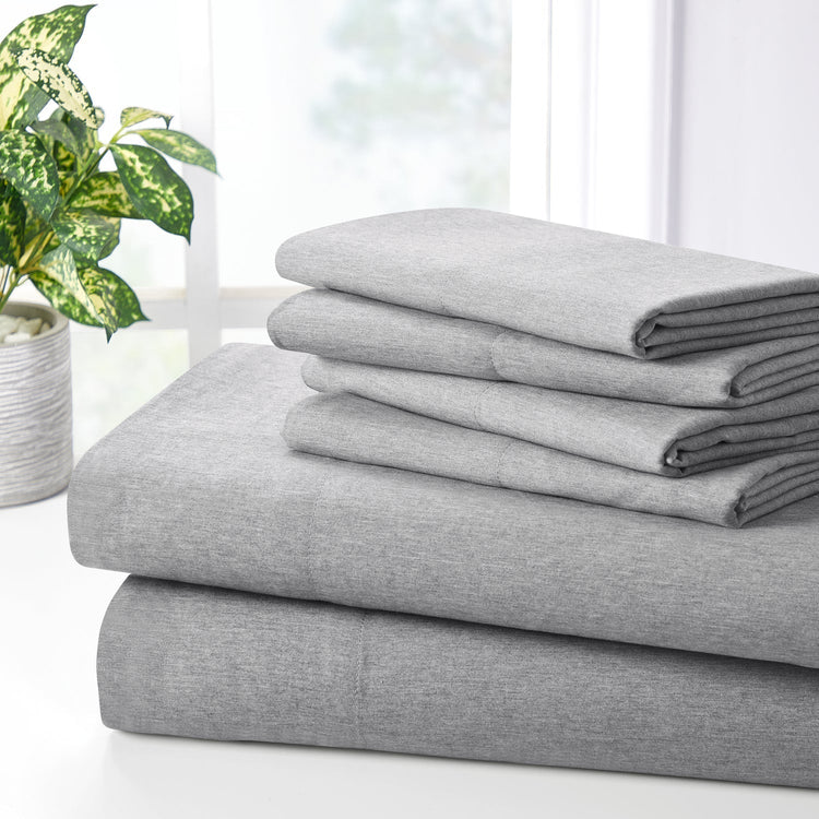 Stack of gray bed sheets on a white surface with a plant in the background