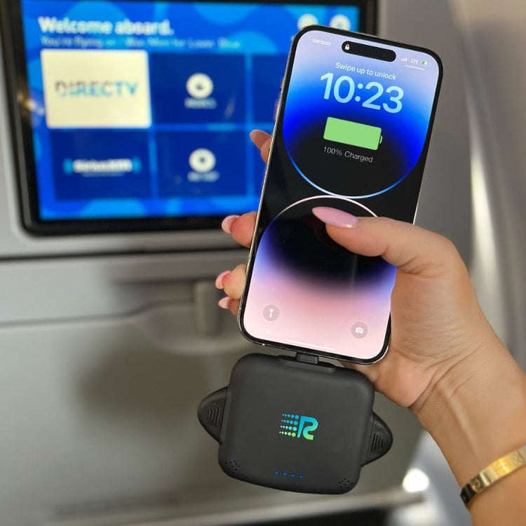 Person holding a smartphone with a wireless charging device on an airplane tray table.