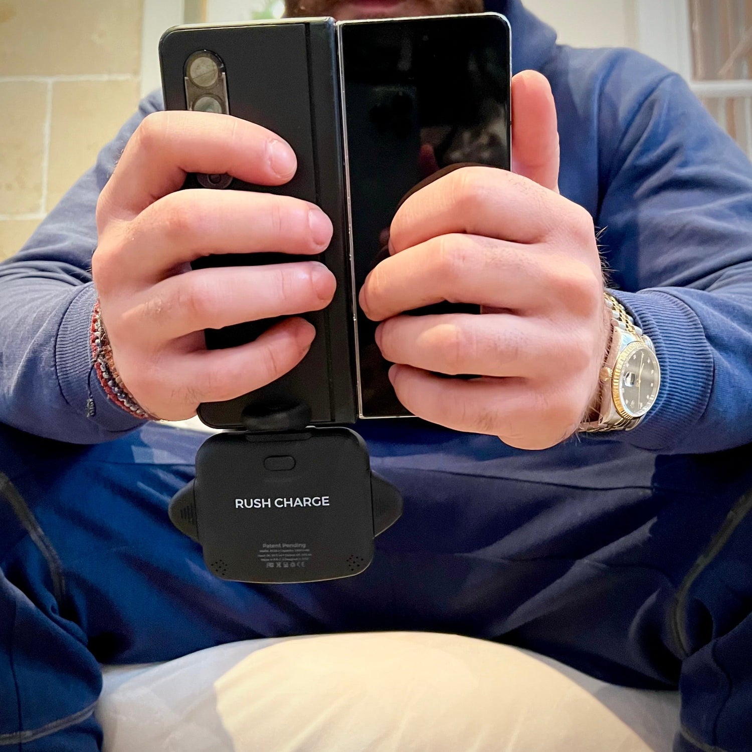 Person holding a dual-screen phone with a 'Rush Charge' device between them.