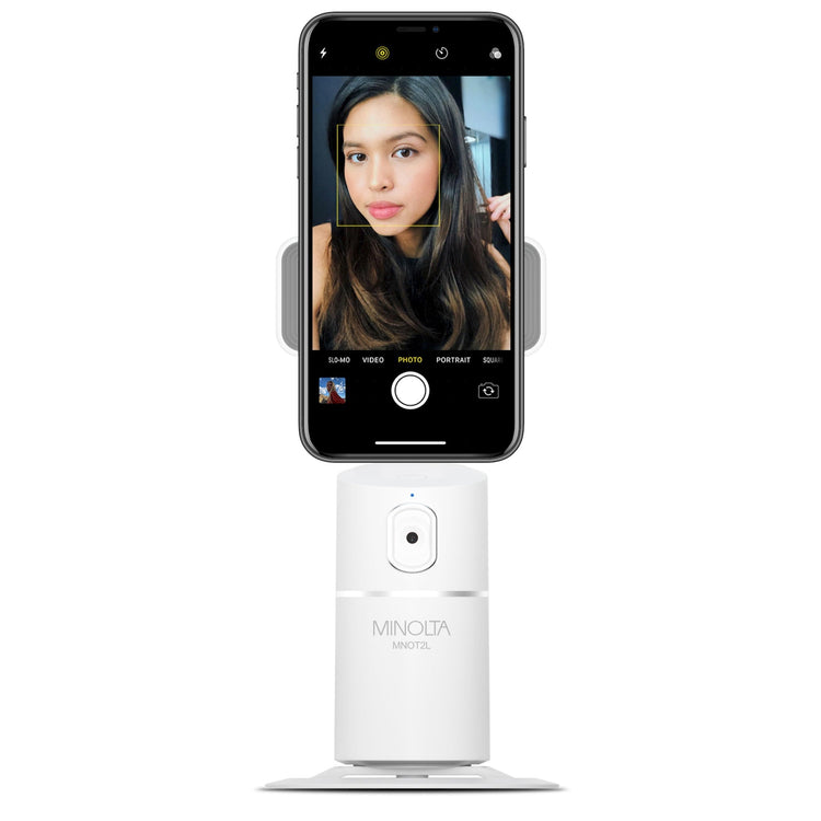 Smartphone mounted on a white stand with a woman's face displayed on the screen, branded 'Minolta'.
