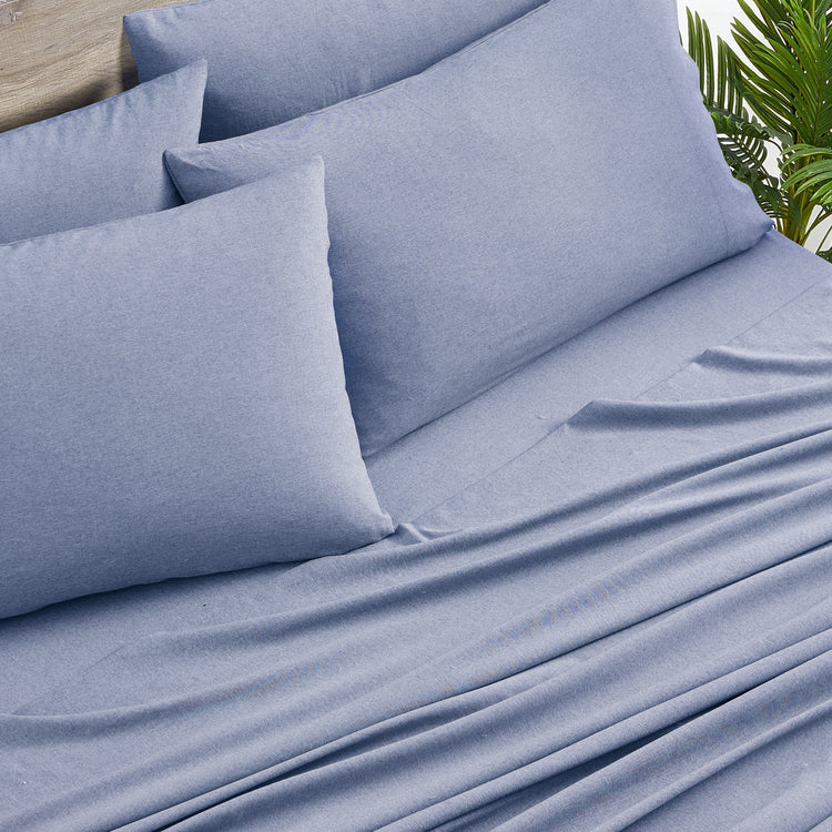 Blue bed sheets and pillows on a bed with a plant in the background