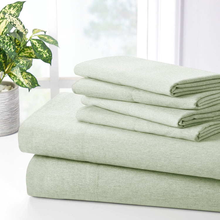 Stack of green bed sheets on a white surface with a plant in the background