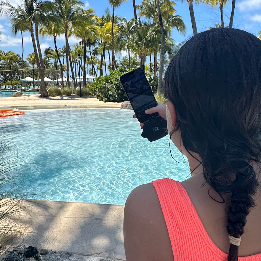 Person taking a photo of a pool with palm trees in the background
