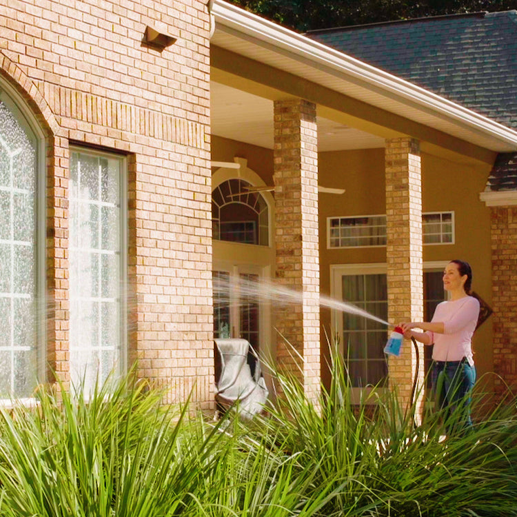 Woman using a pressure washer outside a house with greenery in the foreground