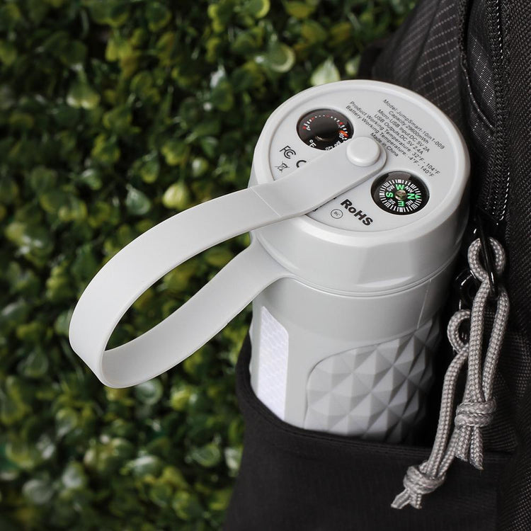 White container with handle and label, attached to a backpack against a green leafy background