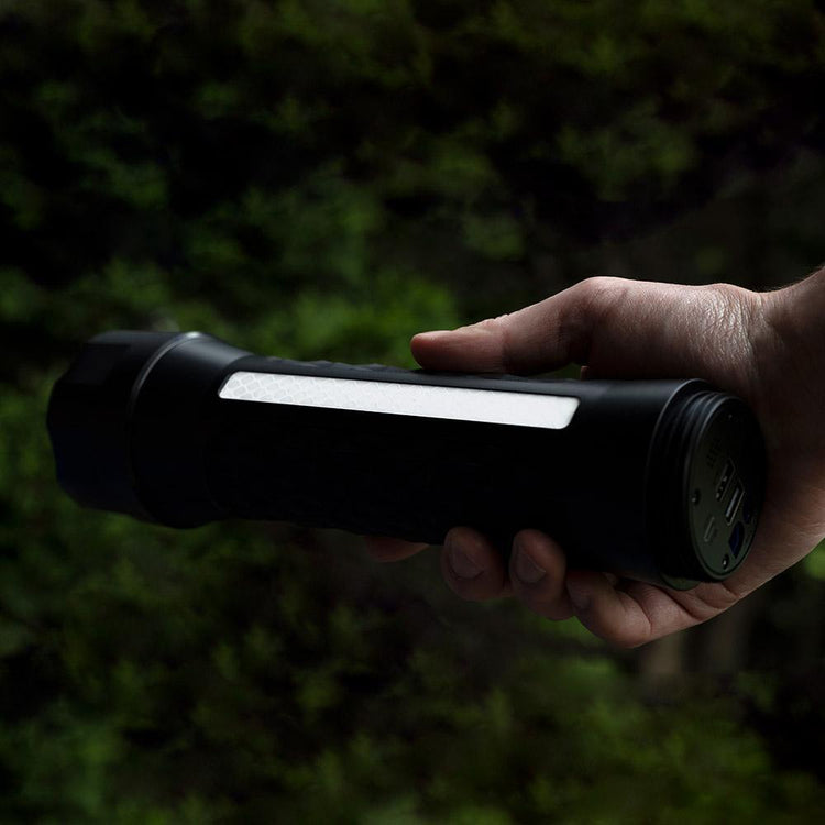 Hand holding a black flashlight with a light on against a dark background