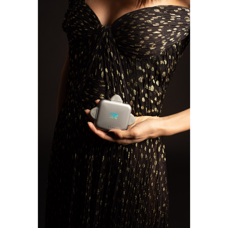 Person holding a small gray device with a logo, wearing a black dress with gold patterns.