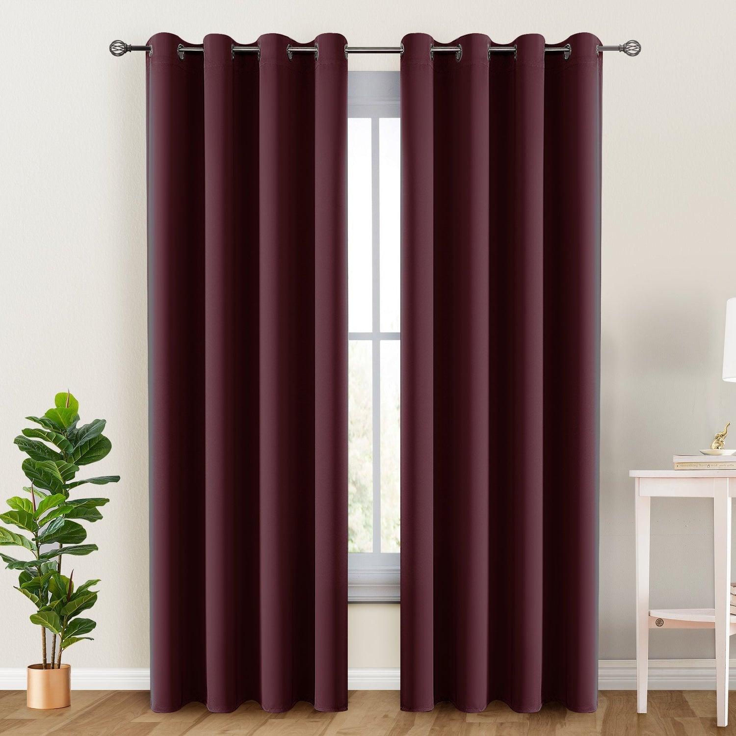 Maroon curtains with grommets on a window, with a plant and table in the foreground.