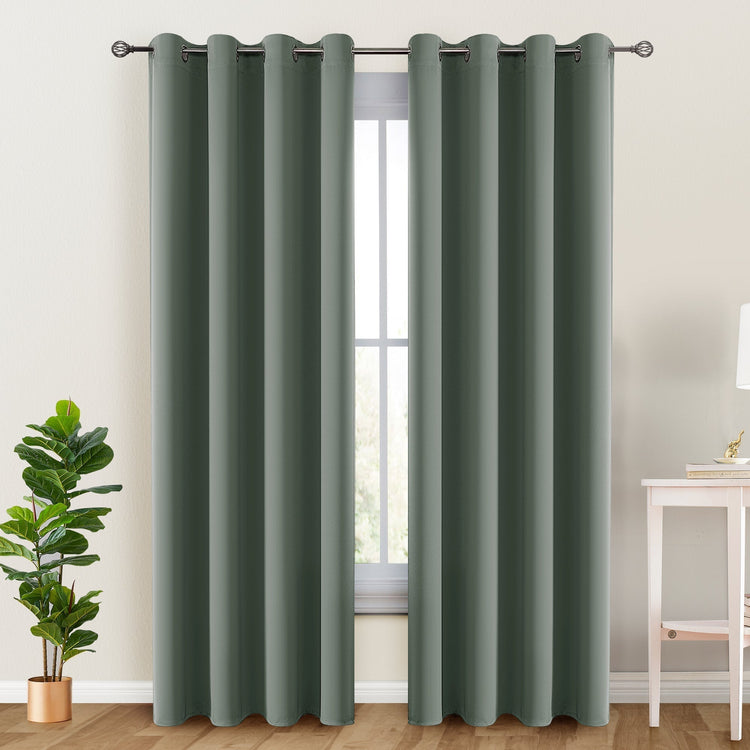 Dark green curtains with grommets on a window, with a plant and table in the background.