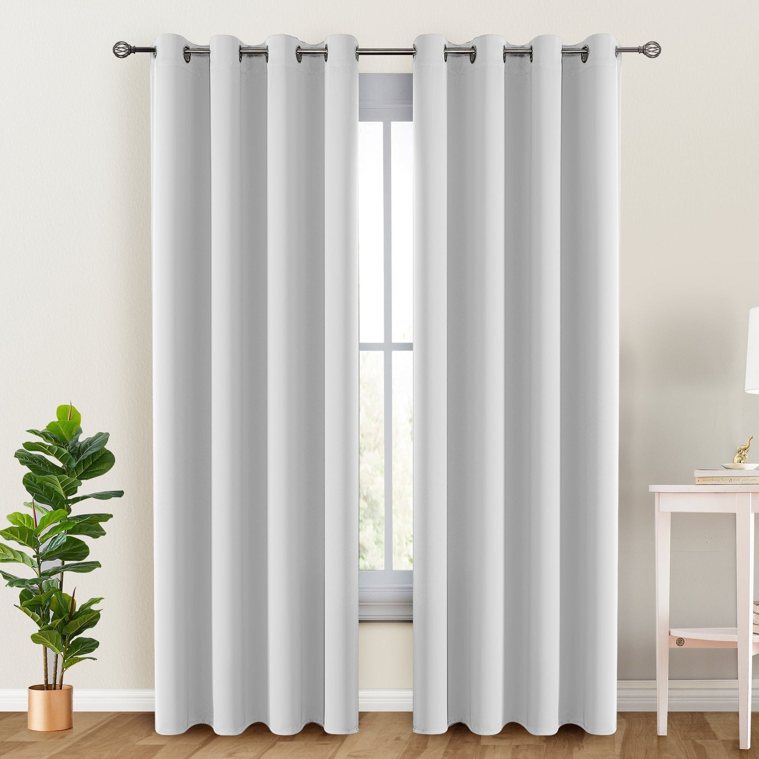 White curtains with grommets on a window, with a plant and table in the foreground.