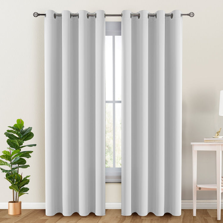 White curtains with grommets on a window, with a plant and table in the foreground.