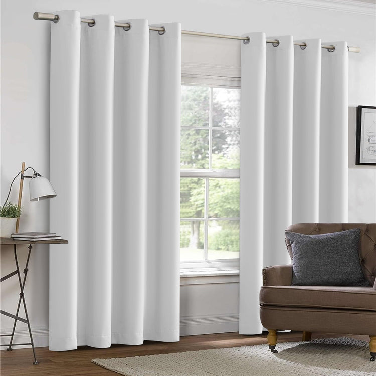 White curtains in a living room with a brown sofa and lamp.