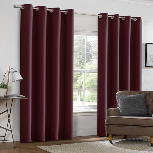 Maroon curtains with grommets on a window, with a plant and table in the foreground.