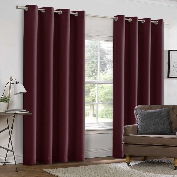 Maroon curtains hanging in a room with a sofa and window.