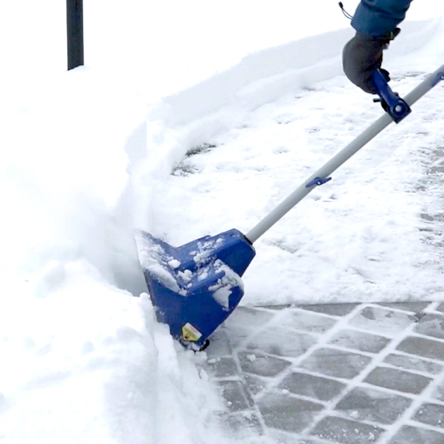 Person using a blue snow shovel to clear snow from a driveway.