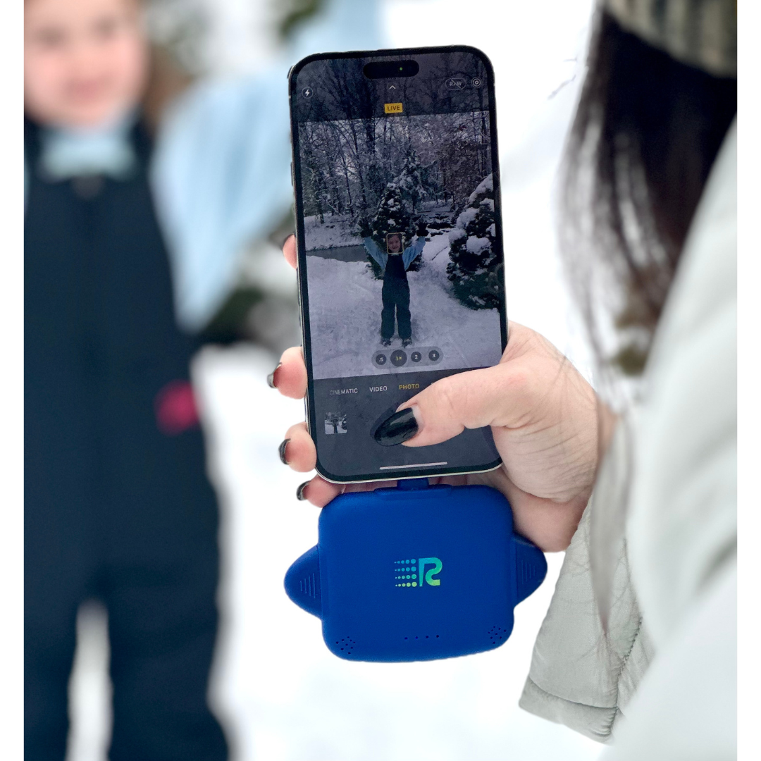 Person holding a phone with a snowy outdoor scene on screen, using a blue device with a logo.