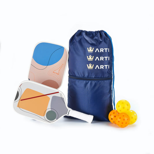 Two pickleball paddles, a blue drawstring bag with 'ART!' branding, and three pickleballs on a white background.