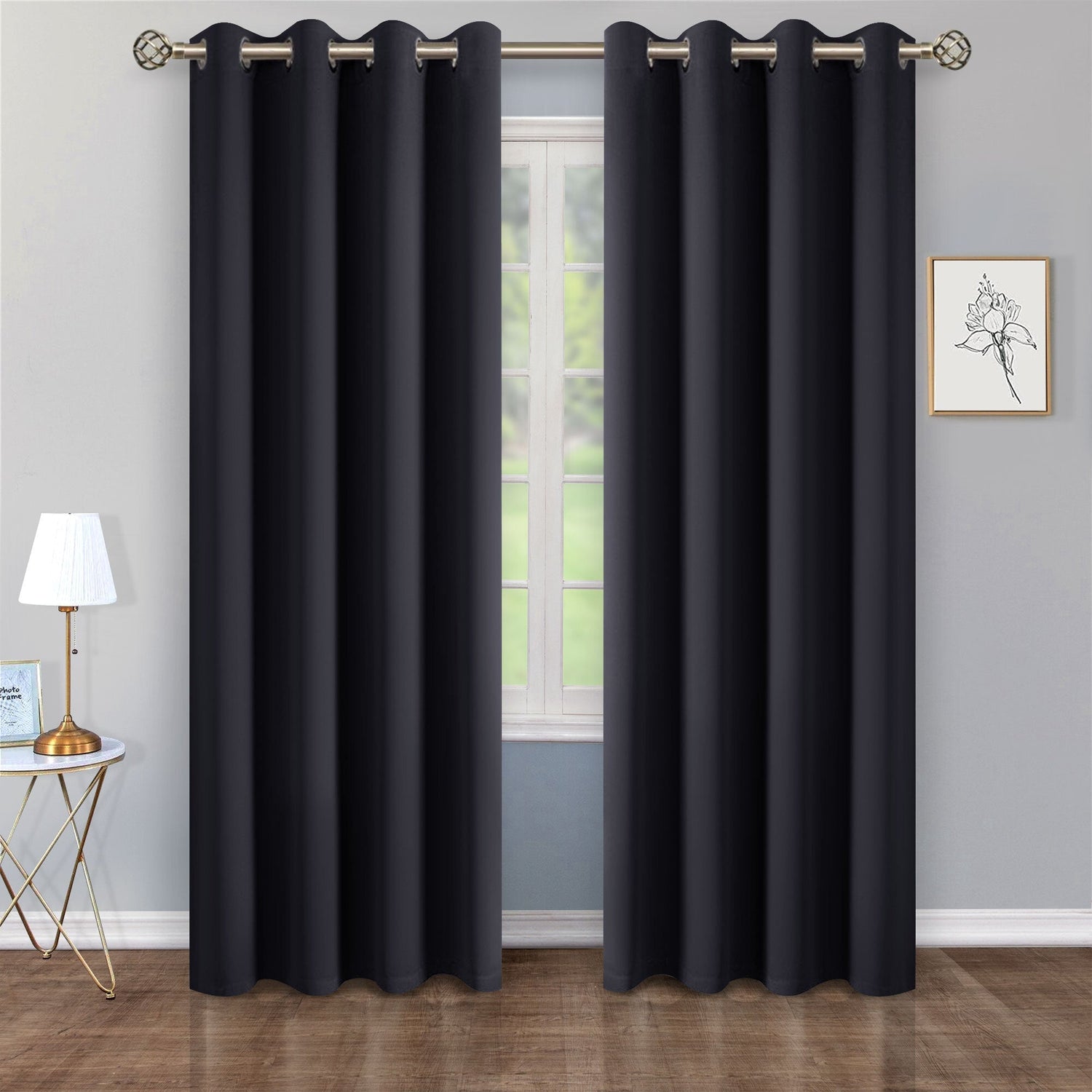 Black curtains hanging in front of a window with a lamp and wall art in the background.