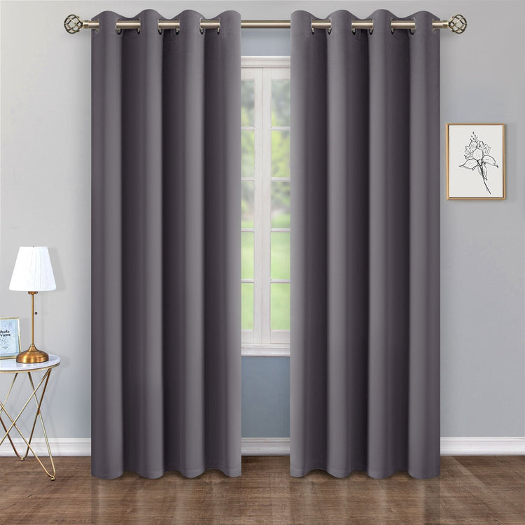 Gray curtains hanging in front of a window with a lamp and wall art in the background.