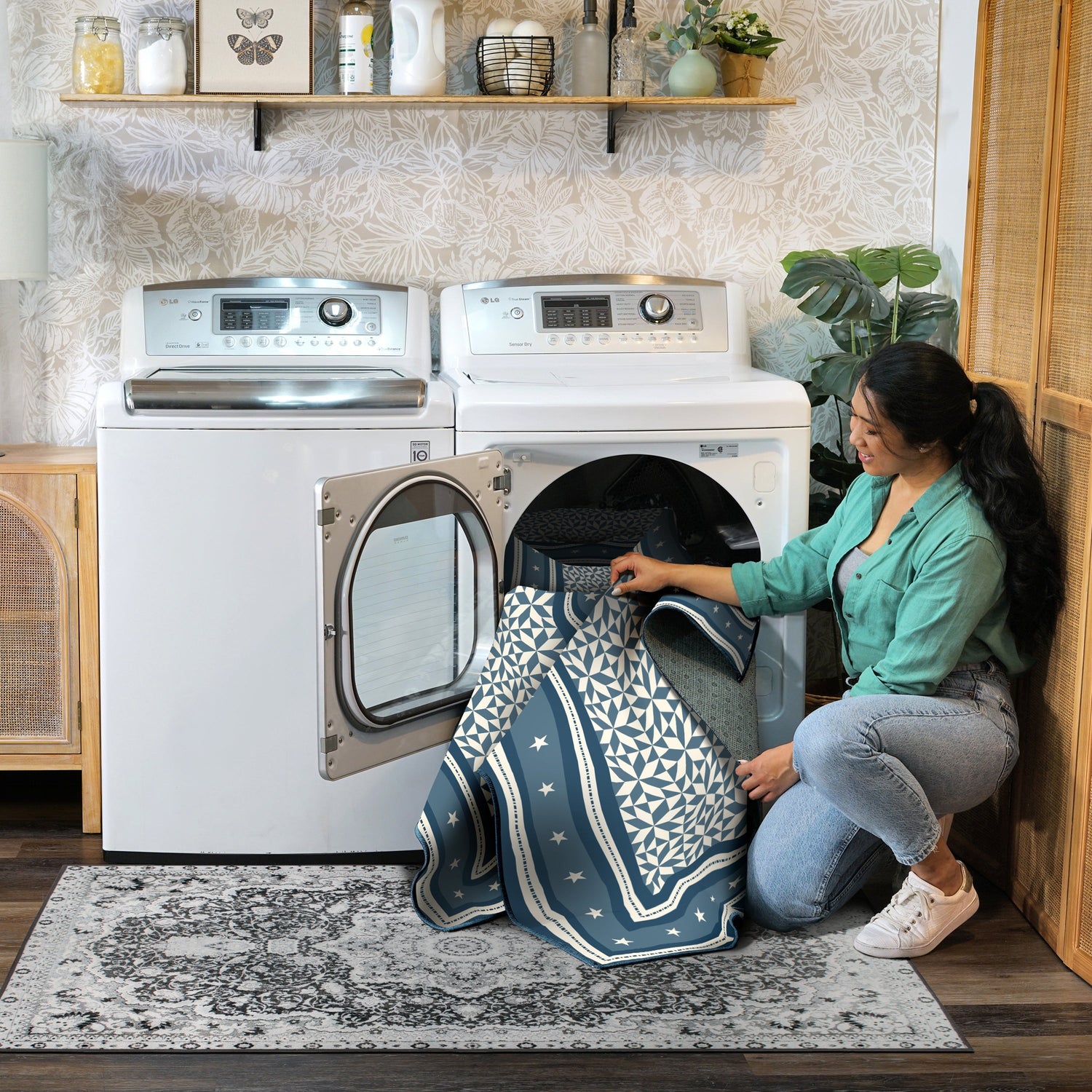 Woman taking a blue and white patterned towel out of a dryer in a laundry room.
