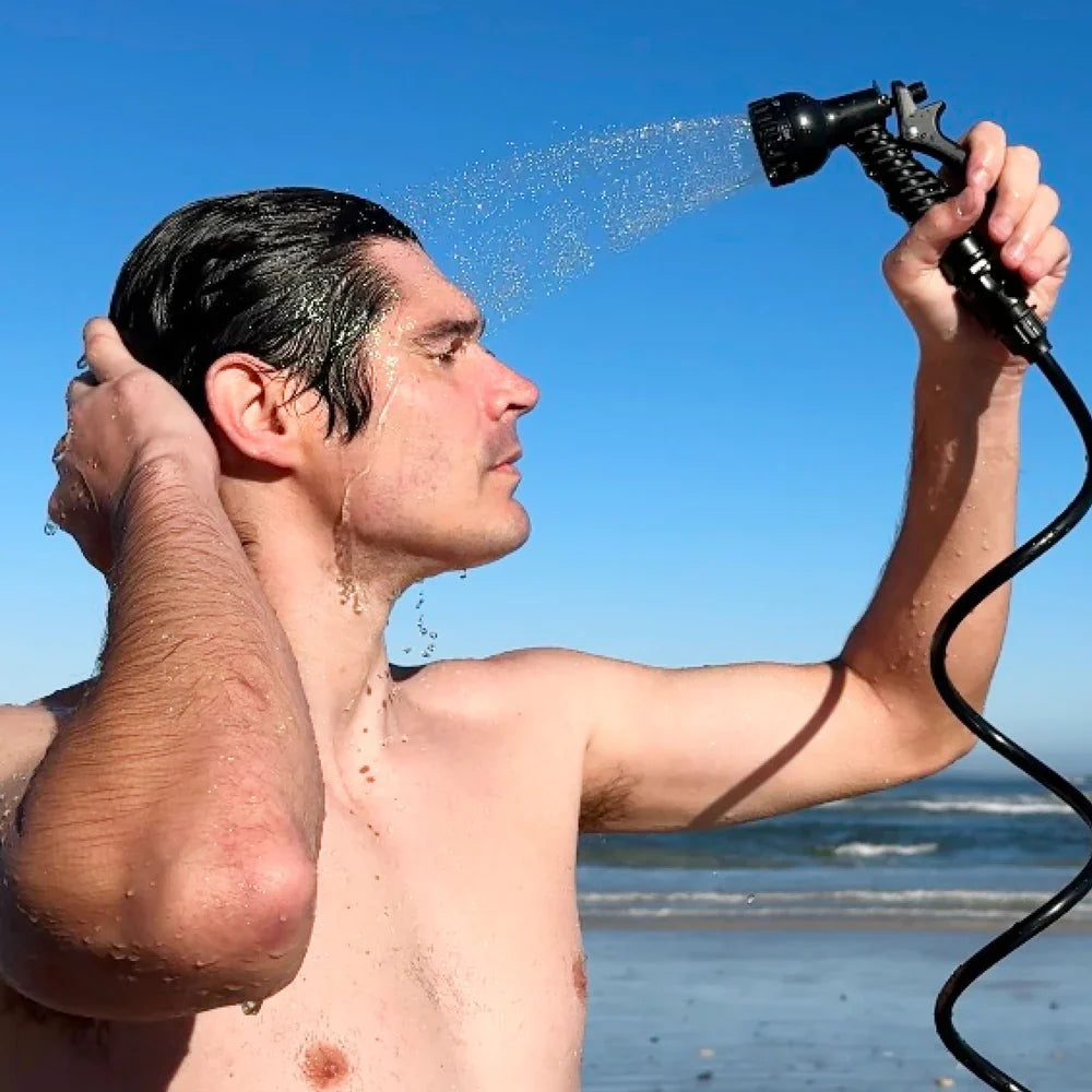 Man showering with a handheld shower head on a beach