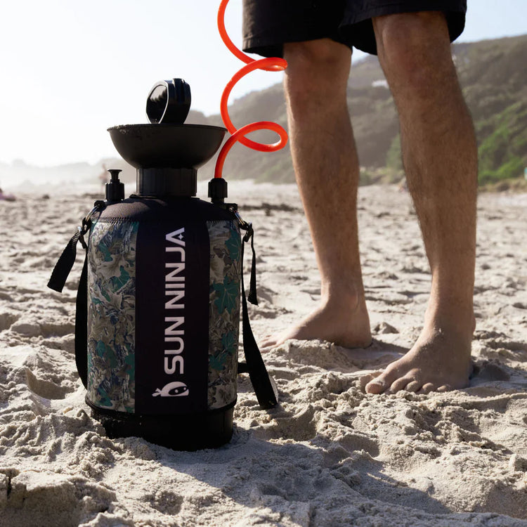 Person standing on a beach with a backpack labeled 'Sunnin' and a red object in the background.