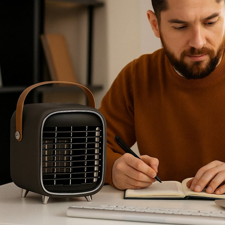 Man sitting at a desk with a laptop, notebook, and small black portable heater.