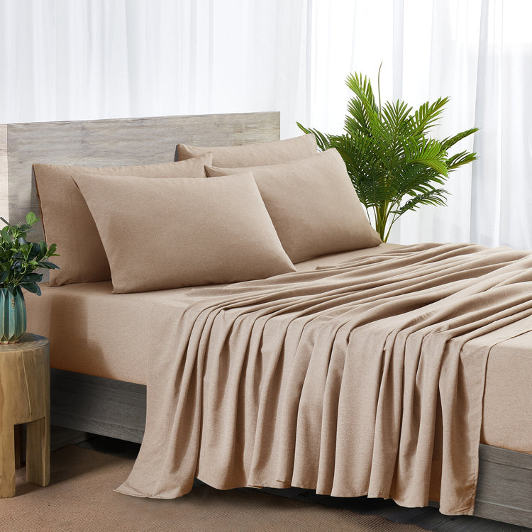 Beige bedspread and pillows on a bed with a plant and side table in the background.