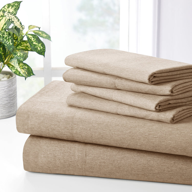 Stack of beige folded bed sheets on a white surface with a plant in the background