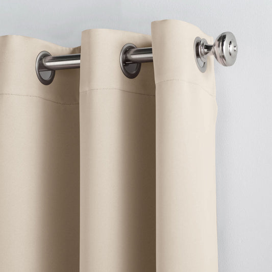 Beige curtains hanging in front of a window with a lamp and wall art in the background.