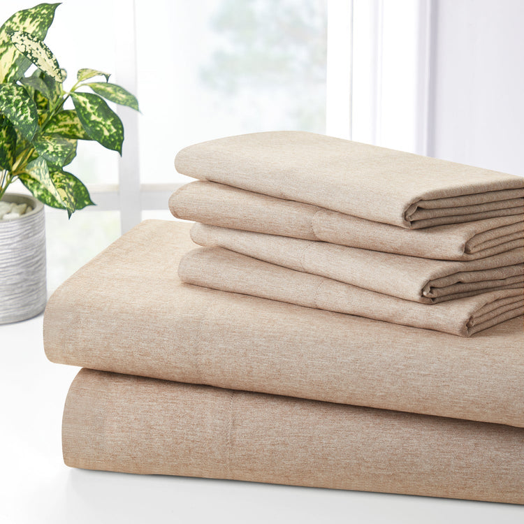 Stack of beige folded bed sheets on a white surface with a plant in the background