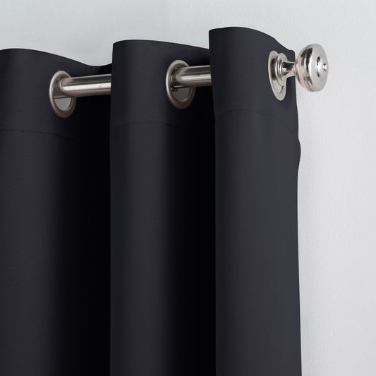 Black curtains hanging in front of a window with a lamp and wall art in the background.