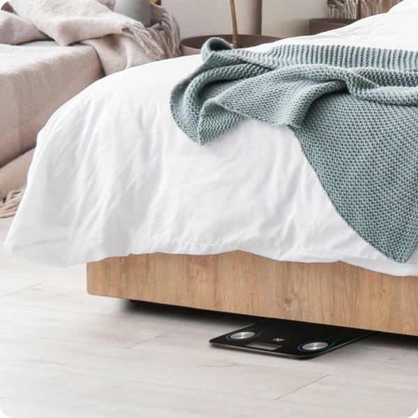 Bed with wooden frame and white mattress, green blanket, and digital scale on floor.