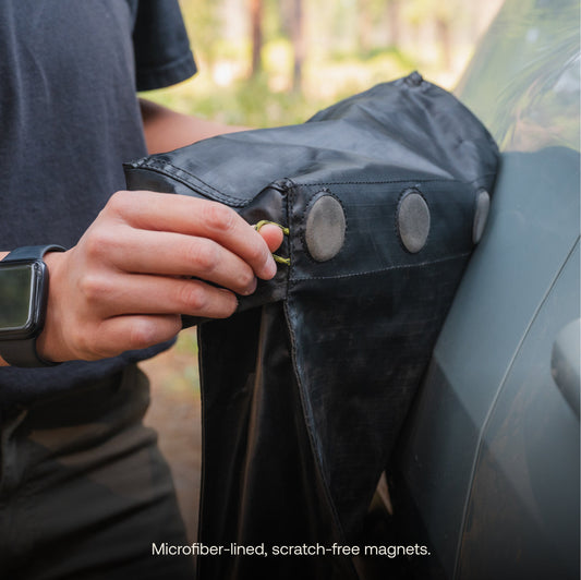 A person puts dirty running shoes with red laces into a black Luno® Gear & Shoe Storage Bag that's attached to the side of a car.