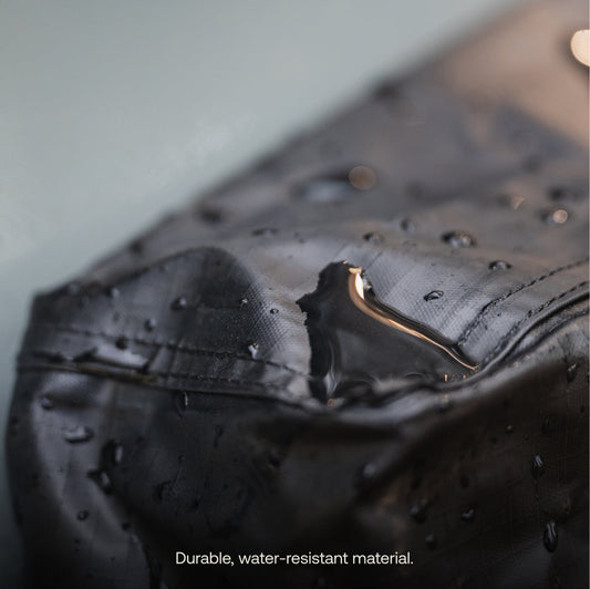 A person puts dirty running shoes with red laces into a black Luno® Gear & Shoe Storage Bag that's attached to the side of a car.