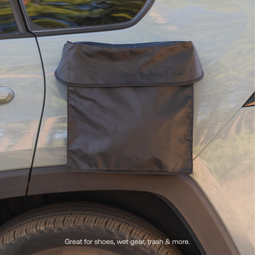 A black Luno® Gear & Shoe Storage Bag is attached to the rear side door of a silver vehicle, offering water-resistant storage for shoes, wet gear, trash, and more.