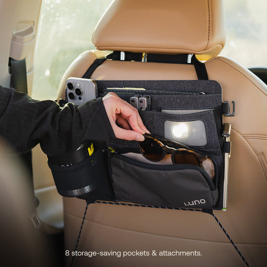 The Luno® Seatback Organizer, a vehicle essential in gray fabric, easily attaches to the back of a beige car seat and features multiple pockets, including mesh and zippered compartments—ideal for car camping adventures.