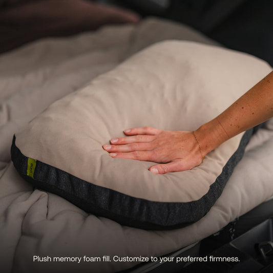 A car’s back seat is converted into a sleeping area with a gray inflatable mattress and Luno® Packable Camping Pillow. The mattress features “DRIVE. CAMP. EXPLORE.”.
