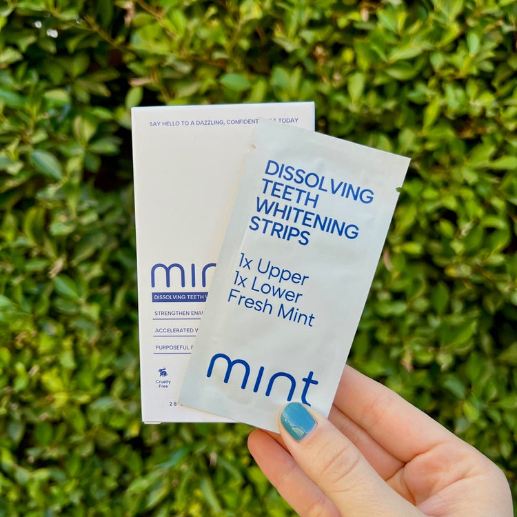 Hand holding two packets of mir teeth whitening strips against a green leafy background