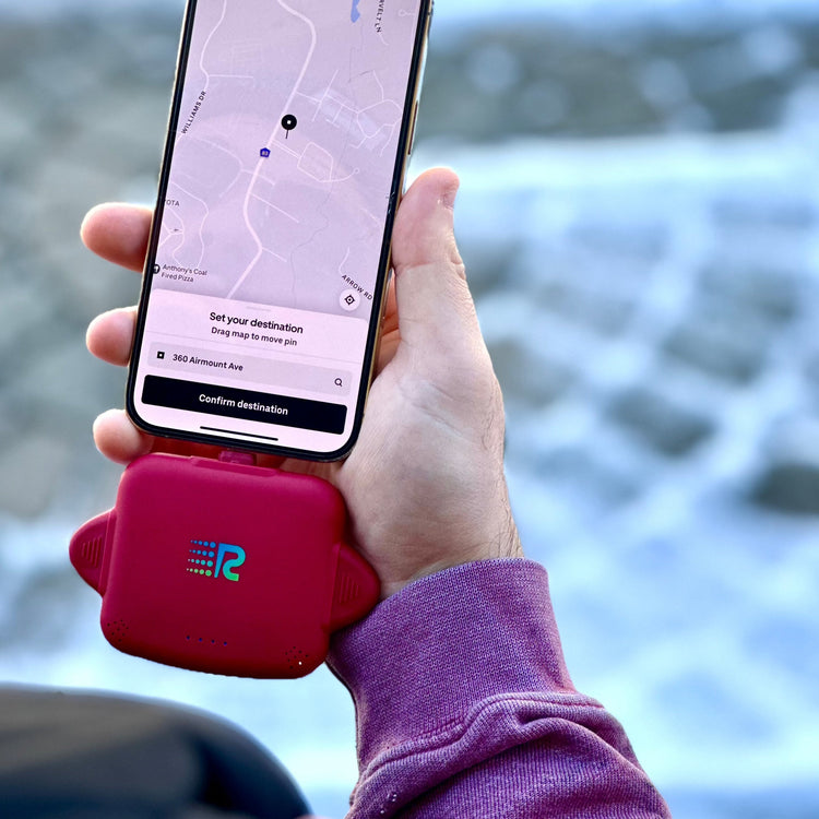 Hand holding a phone with a navigation app, using a red phone holder, with a blurred natural background.