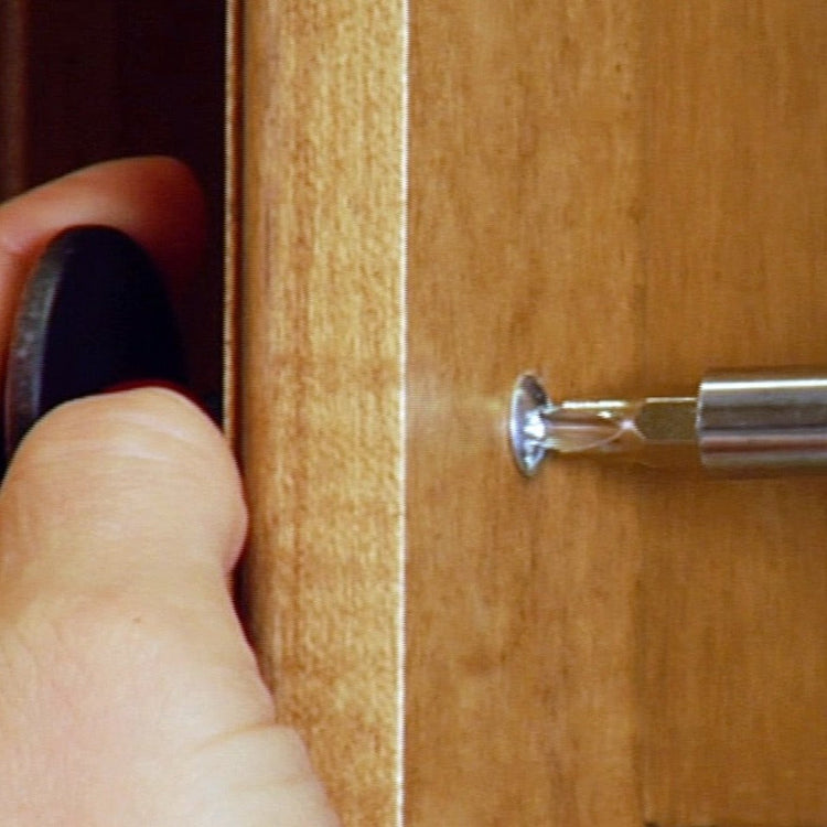 Hand using a screwdriver to remove a screw from a wooden surface