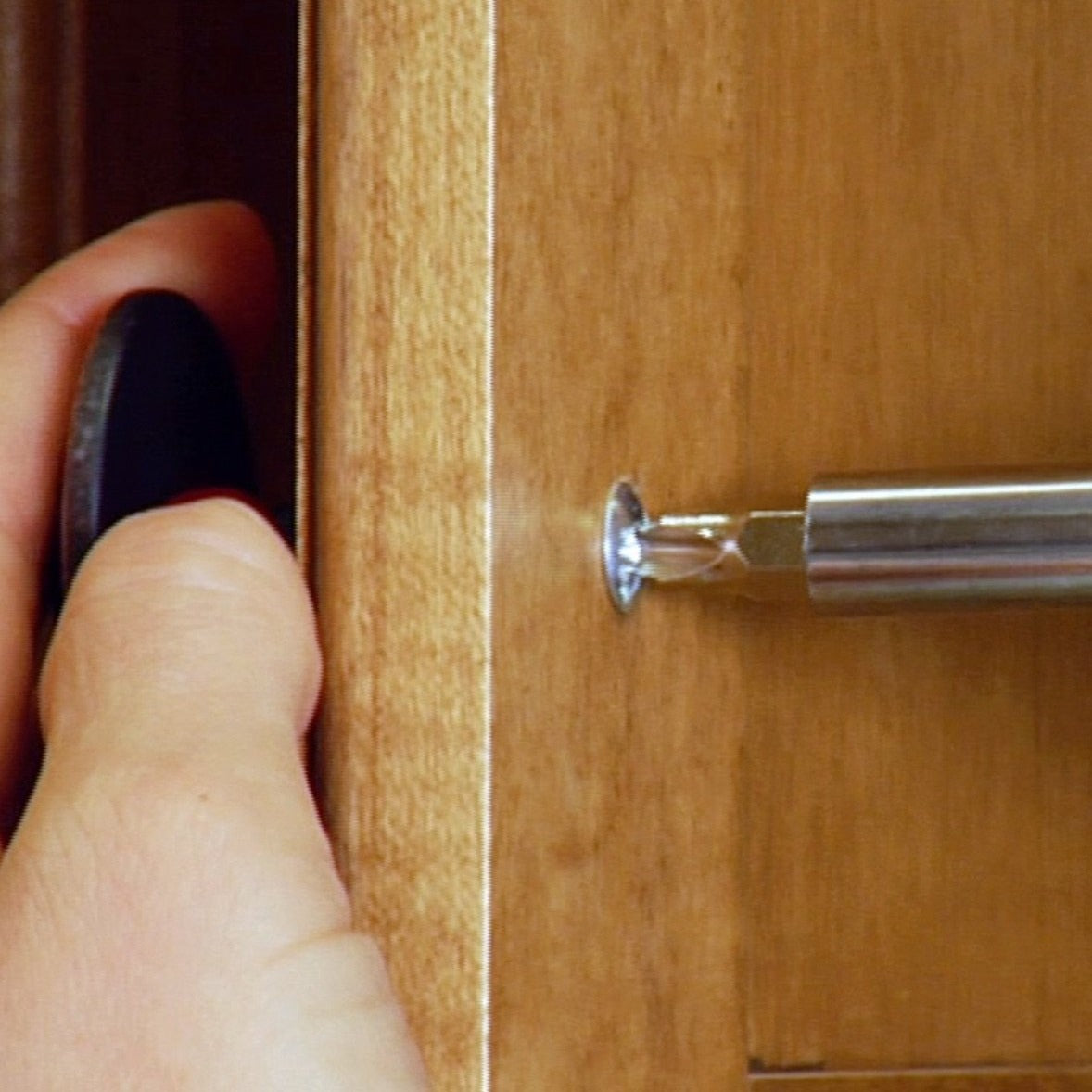 Hand using a screwdriver to remove a screw from a wooden surface