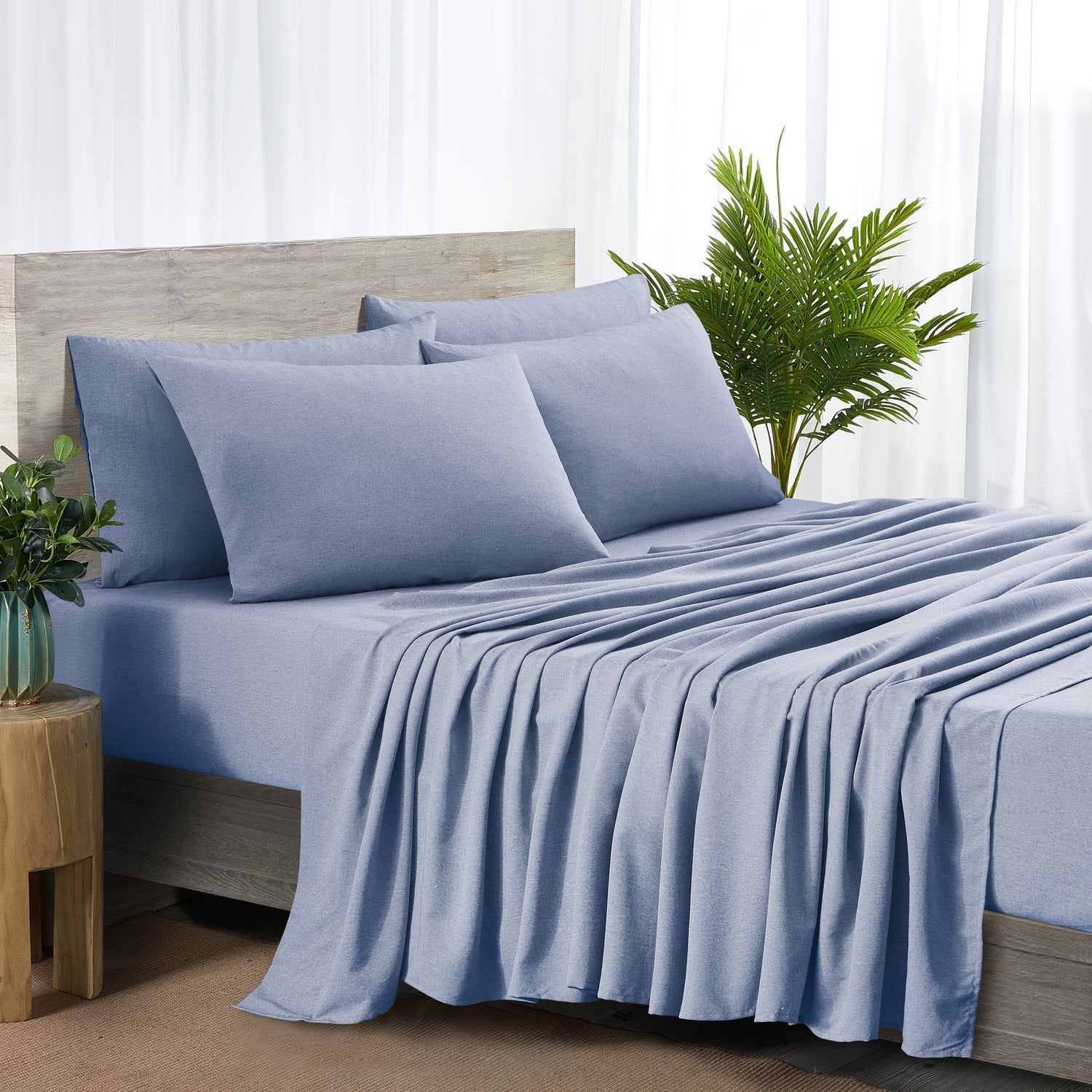 Blue bed sheets and pillows on a bed with a plant and side table in the background.