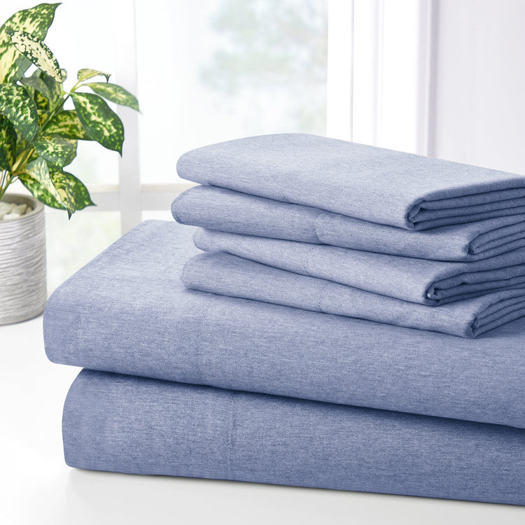 Stack of blue denim-style sheets on a white surface with a plant in the background